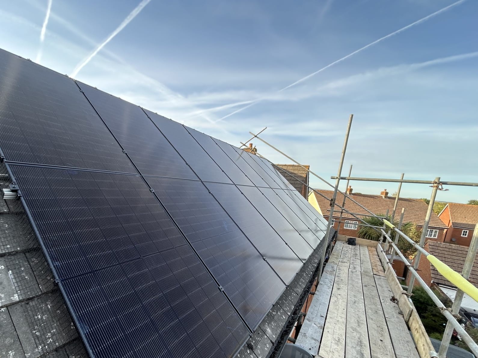 Black solar panels on a slate roof, seen from the installer’s scaffold